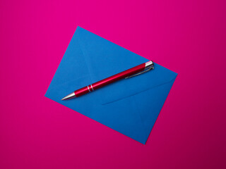 A blue envelope and a red pen on a fuchsia background. Close-up.