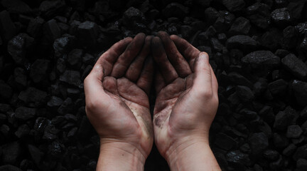 Hands of a miner joined together with some raw coal in the background. Interior of the hands is a...