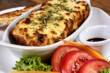 lasagna on white plate with bread and salad