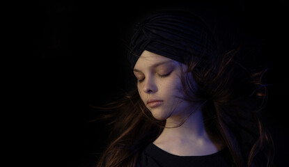 Beautiful little teenager girl with meditative facial expression in multicolor lights. Dark...