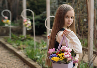 Cute smiling little girl with bouquet of spring flowers in hands outdoor. Portrait of kid with long hair on rural background with seasonal floral gift.