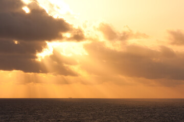 Golden sun rays breaking through clouds above the ocean at sunrise