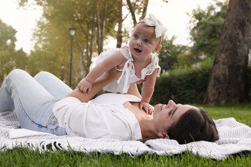 Happy mother with adorable baby lying on green grass in park
