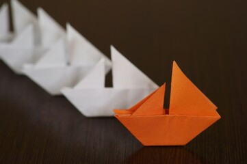 Several white paper boats and an orange one on the table.