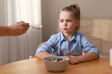 Cute little girl refusing to eat her breakfast at home