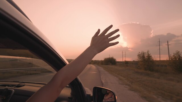girl from a car catches wind with her hand at sunset, drive a car on a journey, drive on an asphalt road, enjoy free speed, happy family life, driver's adventure on vacation, concept of carefree trip