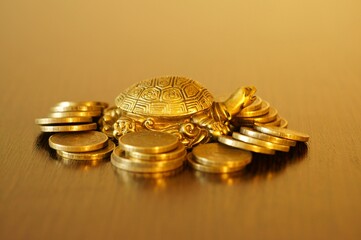 Metal turtle with coins on a gold background. A financial symbol of well-being and stability.