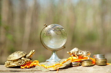 A metal turtle, a glass globe, and a bunch of Chinese coins in close-up.