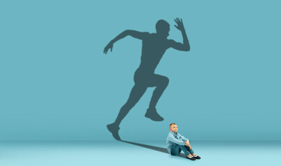 Boy dreaming about big and famous future. Conceptual image with kid and shadow of fit male runner...
