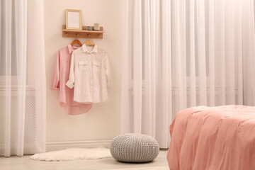 Wooden shelf with fashionable clothes and decorative elements on light wall in bedroom. Interior...
