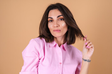 Fototapeta premium Portrait of a young woman in a pink dress on a beige background with shine glitter makeup and cute earrings posing positively, gentle romantic