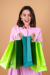 Portrait of a young woman in a pink dress on a beige background with glitter makeup holding shopping packages cute excited