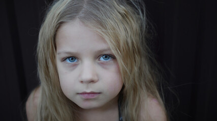 A sad girl with blond hair and expressive eyes looks thoughtfully into the camera.