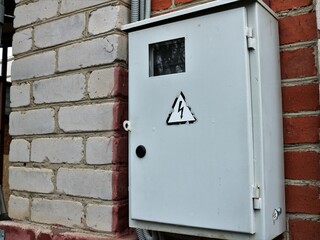 old metal box with electrical wires and energy consumption sensors hanging on the outside brick...