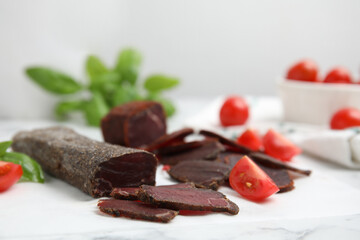 Delicious dry-cured beef basturma with basil and tomatoes on white marble table, closeup