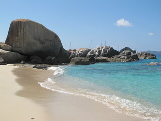 Fototapeta na wymiar Colossal boulder at the beach, surrounded by smaller boulders, stones and rocks. Turquoise sea, blue sky and brown sand. A view of the paradise. Virgin Gorda, British Virgin Islands, Caribbean.