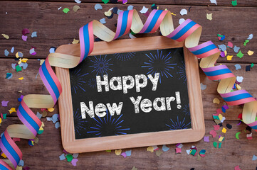 Chalkboard with paper streamers and confetti with happy new year 2022 on wooden background