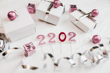 Happy New Year 2022 decorate. Gifts in white boxes with silver wrapping ribbons and pacific pink Christmas balls on a light wooden table