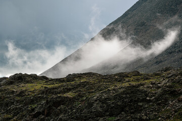 Low clouds, changeable weather in the mountains. Scenic alpine landscape with gray low clouds and sunlight.