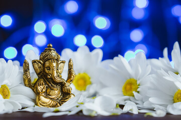 Golden lord ganesha sclupture in daisy flowers over blue illuminated background. Celebrate lord...