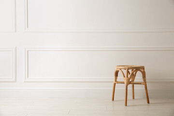 Stylish wooden stool near white wall, space for text. Interior element
