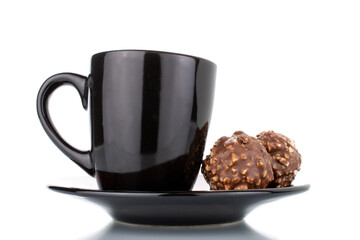 Two sweet chocolate candies with nuts on a ceramic saucer with a cup, close-up, isolated on white.