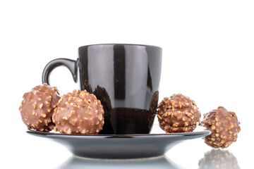 Several sweet chocolate candies with nuts on a ceramic saucer with a cup, close-up, isolated on white.