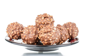 Several sweet chocolate candies with nuts on a ceramic saucer, close-up, isolated on white.