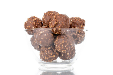 Several sweet chocolate candies with nuts in a glass plate, close-up, isolated on white.