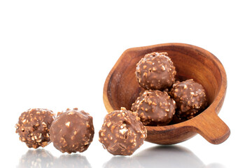 Several sweet chocolate candies with nuts with a wooden cup, close-up, isolated on white.