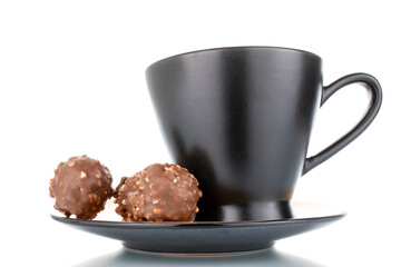 Two sweet chocolate candies with nuts on a ceramic saucer with a cup, close-up, isolated on white.
