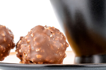 Two sweet chocolate candies with nuts on a ceramic saucer with a cup, close-up, isolated on white.
