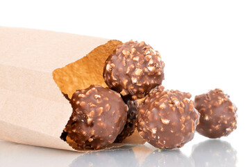 Several sweet chocolate candies with nuts in a paper bag, close-up, isolated on white.