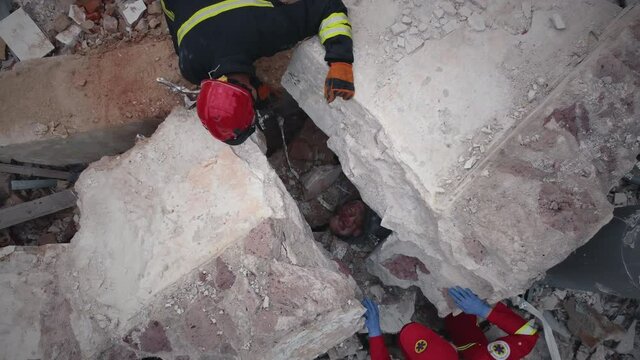 Zoom out aerial view of emergency service workers hurrying to save person buried under rubble of demolished concrete building after earthquake