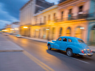 Caribbean, Cuba, Havana, Havana Vieja (Old Havana), a UNESCO World Heritage Site, classic car in motion at dusk