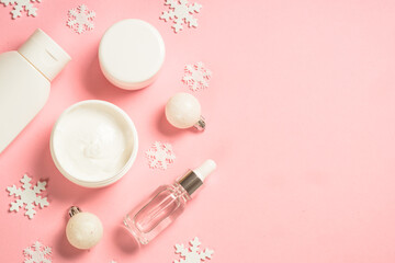 Winter cosmetic, skin care product at pink. Cream, serum, tonic with winter decorations. Top view with copy space.