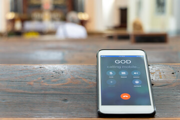 Calling God with a mobile phone on the table of a prayer bench in the church with altar.