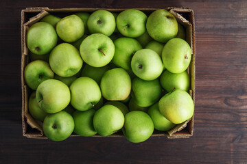 Green apples in a box on a wooden table, top view.