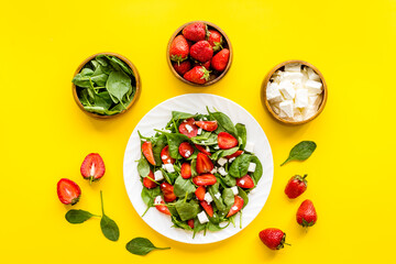 White plate of green spinach salad with strawberry and goat cheese