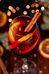 A glass of mulled wine on the wooden table surrounded by Christmas decorations close up. Festive winter drink vertical photo