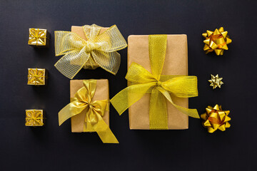 A set of gifts for Christmas, New Year, Birthday in gold and craft paper with different bows on a black background. Flat lay, top view