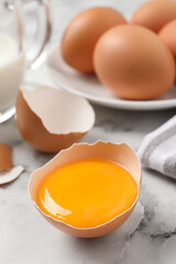 Cracked eggshell with raw yolk on white marble table, closeup. Space for text