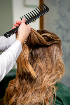 A female hairdresser is combing the long brown hair of a young woman at a parlor