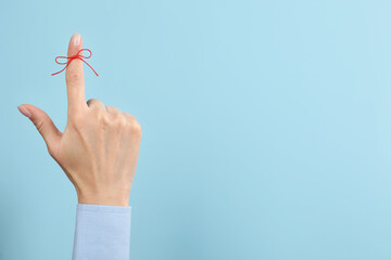 Woman showing index finger with tied red bow as reminder on light blue background, closeup. Space for text