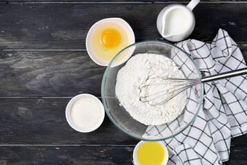 Pancake ingredients. Ingredients for baking: eggs, butter, sugar, milk, whisk, textiles on a wooden background with copy space. Baking ingredients background.