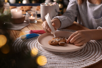 Little child decorating Christmas cookie at wooden table, closeup