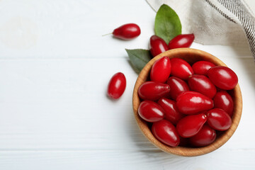 Fresh ripe dogwood berries with green leaves on white wooden table, flat lay. Space for text