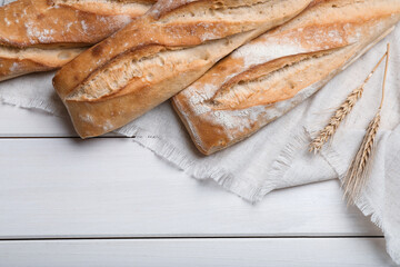 Tasty baguettes and spikelets on white wooden table, flat lay. Space for text