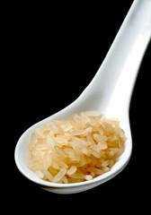 White china spoon with raw rice over black background