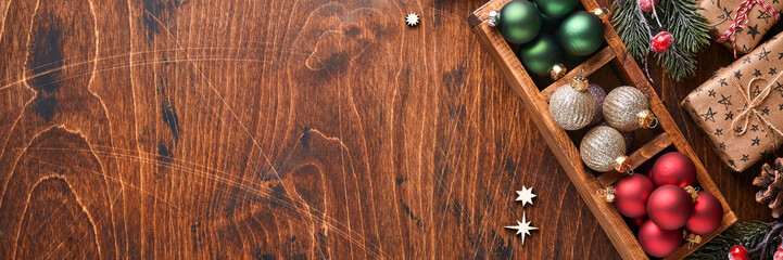 Fir tree decor red and green Christmas balls, shaped cinnamon and dry oranges slices on wood background for your xmas greetings. Top view with copy space. Christmas greeting card.